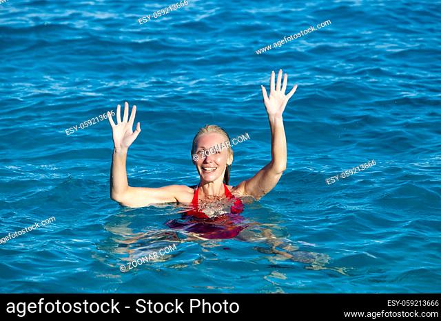 The young woman in a red bathing suit on sea background greeting waving