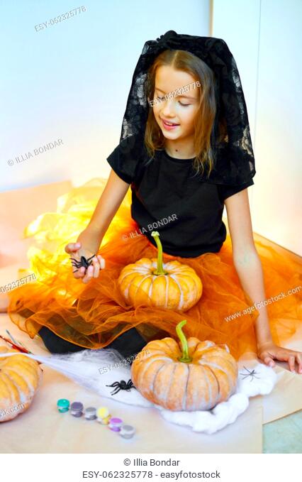 Child play with spider, decorating a pumpkin at home, Little girl drawing face on orange Halloween Jack-O-Lantern pumpkin. Holiday decoration concept