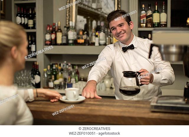 Smiling barkeeper preparing cup of coffee for woman