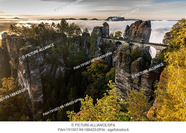 07 October 2019, Saxony, Dresden: In the morning fog lies over the Saxon Switzerland National Park behind the bastion bridge built in 1851 and the...