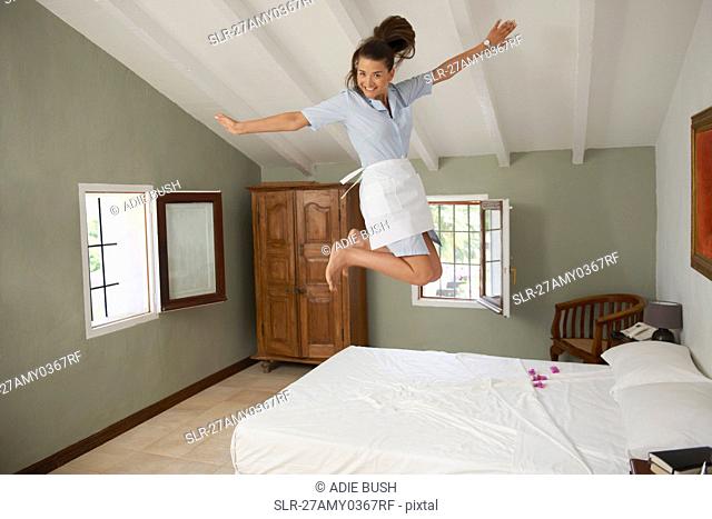 Hotel maid jumping on bed in room