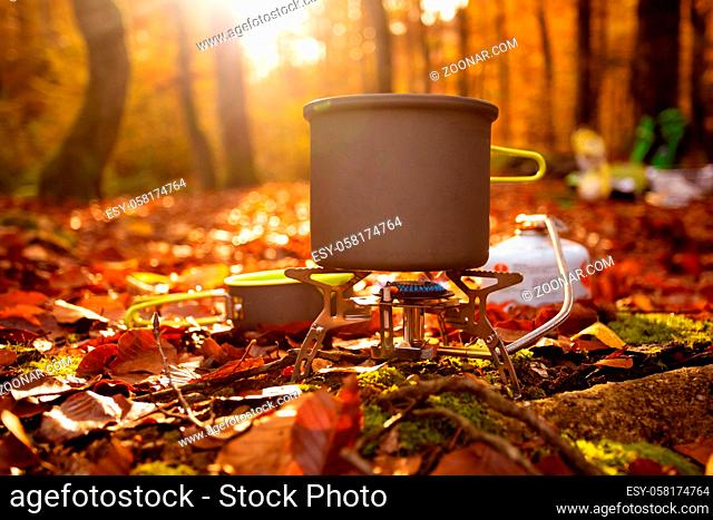 Grey portable camping kettle on a portable gas stove. Cooking while camping late autumn. Beautiful autumn forest scenery on a background blured