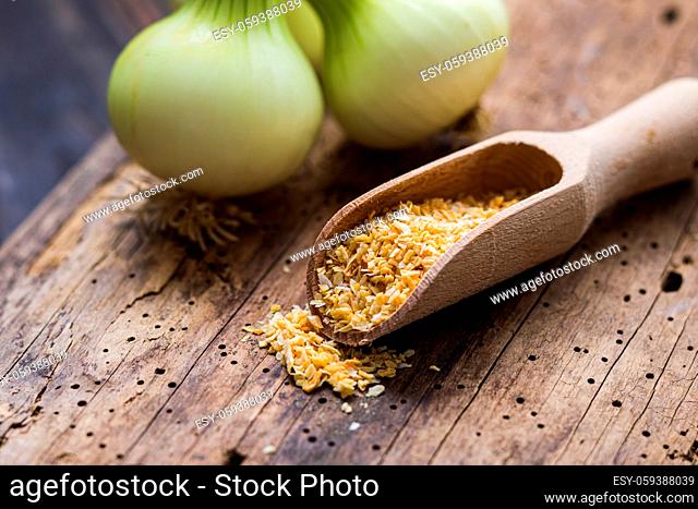 Closeup view dried up and ground onions in spice scoop, fresh onions on background, blured. Old crannied wooden table