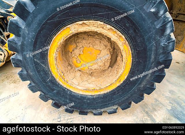 Close up view of the heavy duty black rubber tire of a construction vehicle. Caked mud can be seen on the yellow wheel rim and body of the machinery