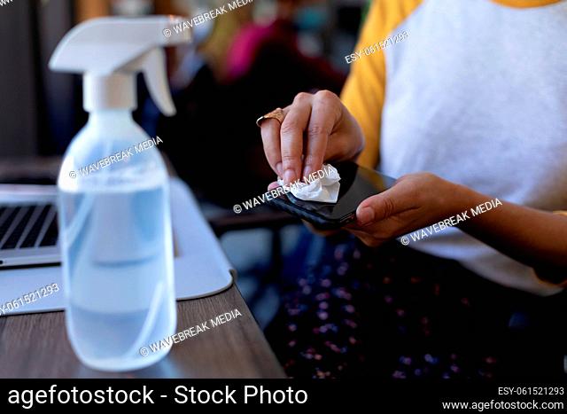 Mixed race woman disinfecting her smartphone in an office