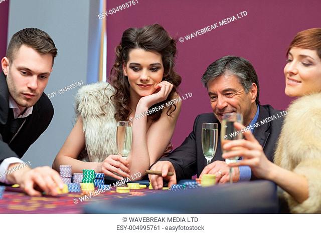 People sitting at the table looking while man placing a bet
