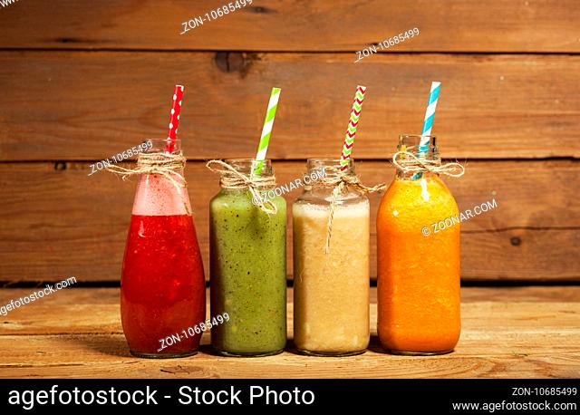 Assortment of fruit and vegetable smoothies in glass bottles with straws on wooden background