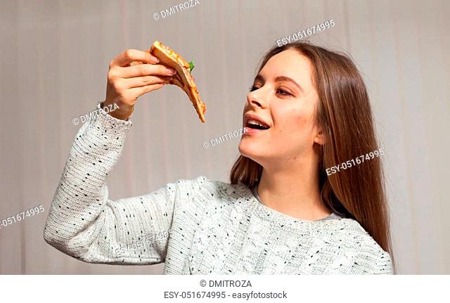 Pretty woman is keeping a slice of pizza in her hand and going to eat it