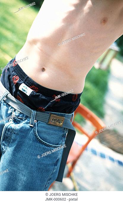 A boy, teenager, in the garden is showing his belly, upper part of the body