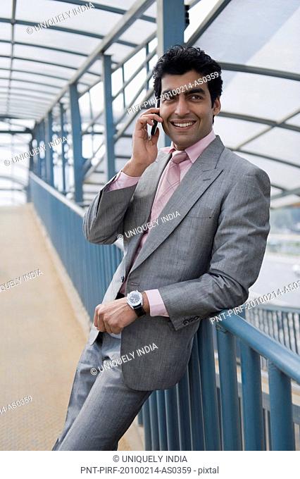 Businessman talking on a mobile phone on a footbridge, Gurgaon, Haryana, India