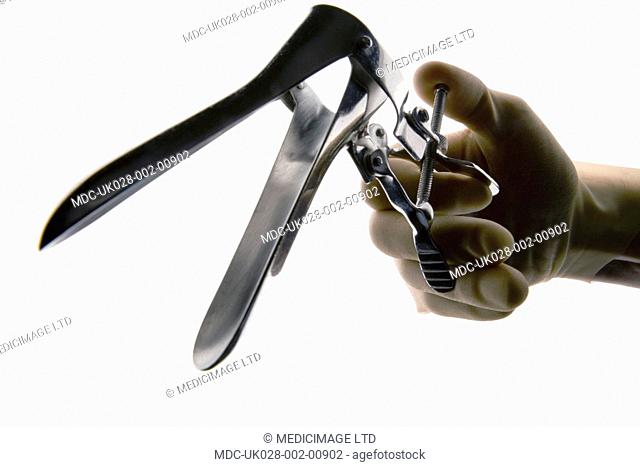 Gloved hand holding a vaginal speculum. The vaginal speculum is used as a medical tool to hold open the vagina during medical investigation