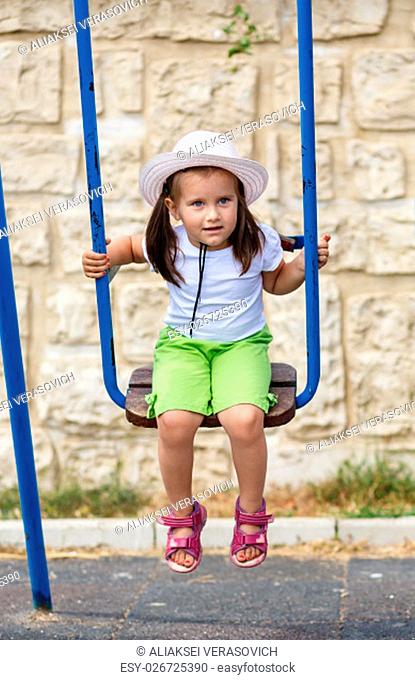 Baby girl on a swing. Child in a white hat to play outdoors