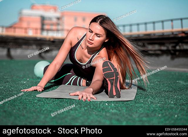 Fitness on the roof, sporty woman stretching. Young female with long hair, training on the roof of the building in the city