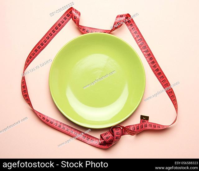 green round plate and red measuring tape on a beige background, weight loss concept, flat lay