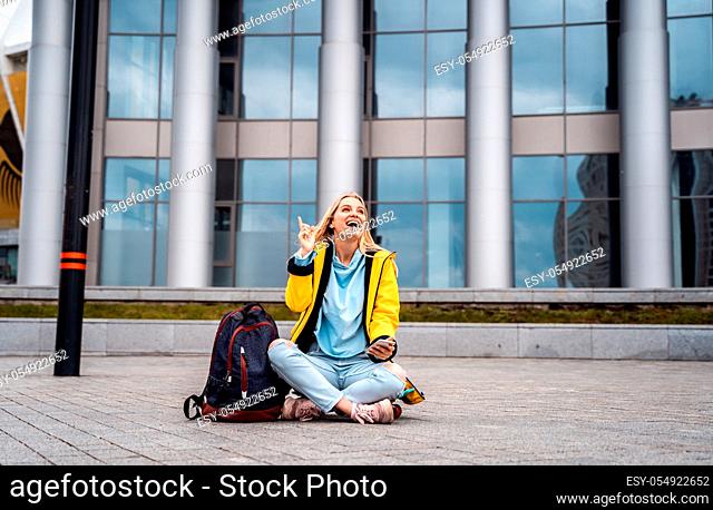 Beautiful girl calls by phone and sits on skateboard, against the background of the street