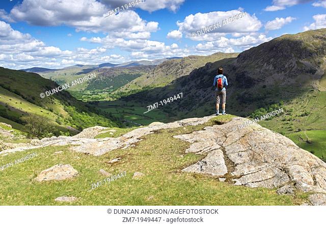 A hiker looks out over Seathwaite valley from Sour Milk Gill on a sunny day in the Lake District, UK