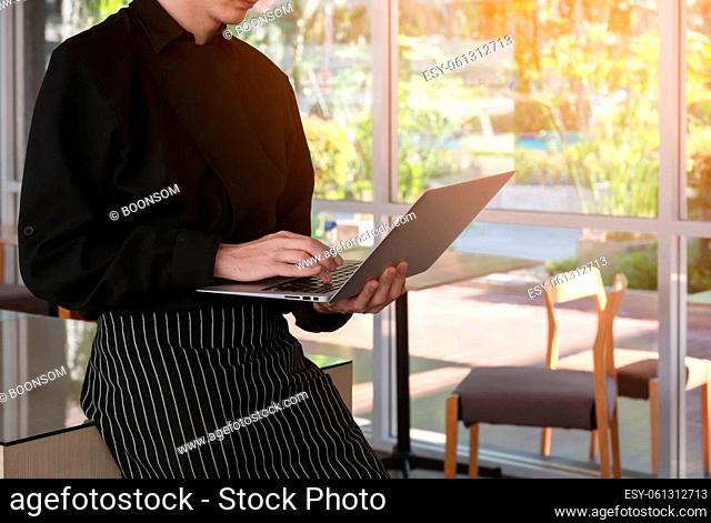 Barista in black apron using laptop while standing in cafe, coffee shop business