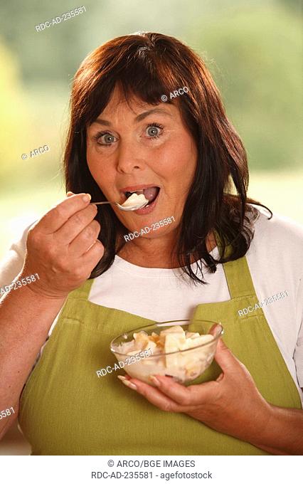 Woman with bowl of fruit salad with yoghurt / spoon, testing