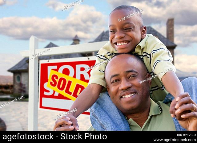 Happy african american father and son in front of new home and real estate sign