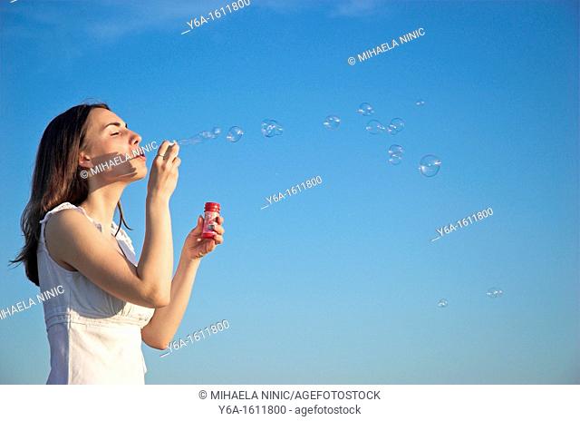 Young woman blowing bubbles against blue sky, close-up