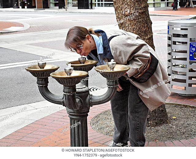 A mature woman drinks from a fountain on a downtown sidewalk in Portland, Oregon  Known as Benson Bubblers these fountains, unique to Portland