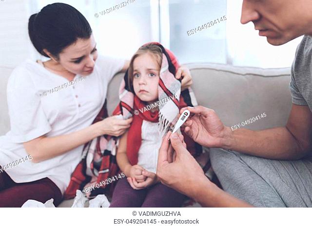 The little girl caught a cold. Her mother and father are treating her. Father measures the girl's temperature. The mother sits next to her and worries about it