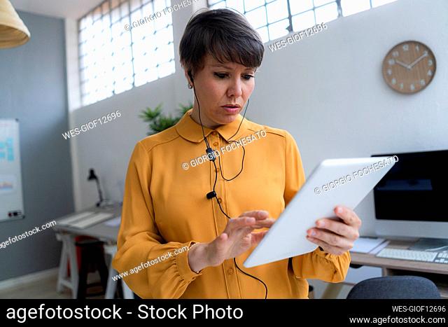 Businesswoman wearing in-ear headphones using digital tablet while working in office