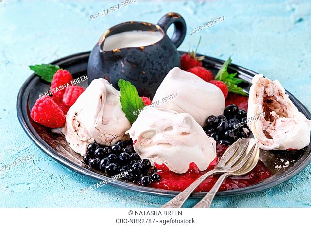 Traditional summer dessert Eton Mess. Meringue, jug of cream, berry jam, fresh blueberries, raspberries on vintage tray, decorated with mint leaves over light...