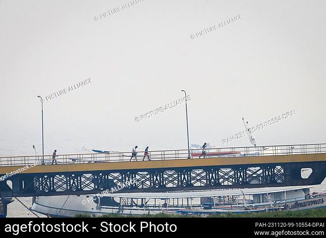 PRODUCTION - 02 November 2023, Brazil, Parintins: People walk across a bridge at the harbor amid heavy smoke caused by a forest fire