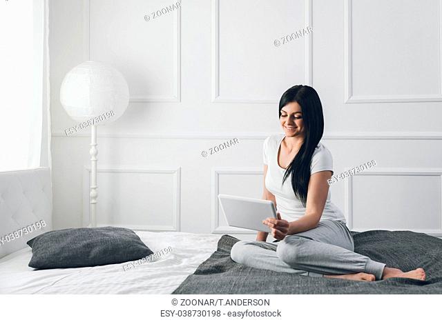 Beautiful young woman relaxing on the bed and using her tablet