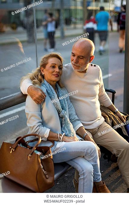Spain, Barcelona, senior couple with baggage sitting at tram stop in the city
