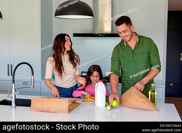 Happy caucasian parents and daughter unpacking groceries in kitchen
