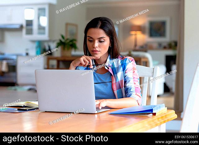 Caucasian woman sitting by desk working from home using laptop