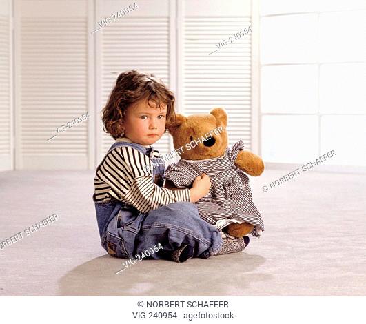 portrait, sad girl with brown hair, 4 years, sits with her stuffed bear on the floor in the living room  - GERMANY, 25/05/2003