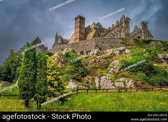 Trees and meadow at foothill of Rock of Cashel, known as Cashel of Kings or St. Patricks Rock with dramatic storm clouds, County Tipperary, Ireland