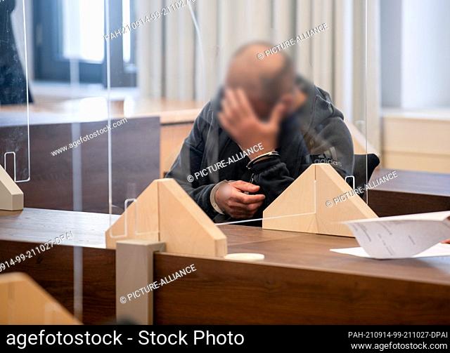 14 September 2021, Bavaria, Memmingen: In the district court, a man sitting in the dock with his hands cuffed holds his hands in front of his face