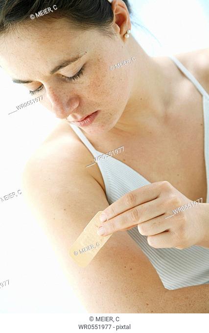 young woman is sticking a plaster on her upper arm -band-aid