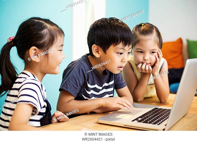 Three children using a laptop, two girls and a boy