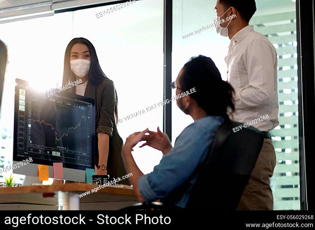 Three asian business person discuss their work in morning after office reopen due to coronavirus COVID-19 pandemic. They wear protective face mask to prevent...