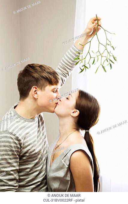 Man kissing woman while holding mistleto