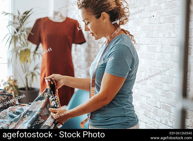 Woman in tailor activity at home or design studio store. Workshop of tailoring. Adule female working with textile and mannequin in background
