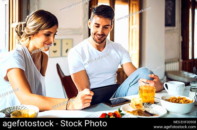 Young couple watching tablet while having breakfast at home