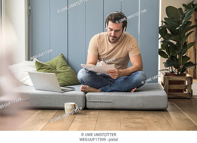 Young mamn sitting on mattress, taking notes, using headphones