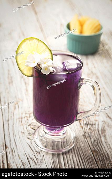 A refreshing glass of butterfly pea flower tea with ice and a lime