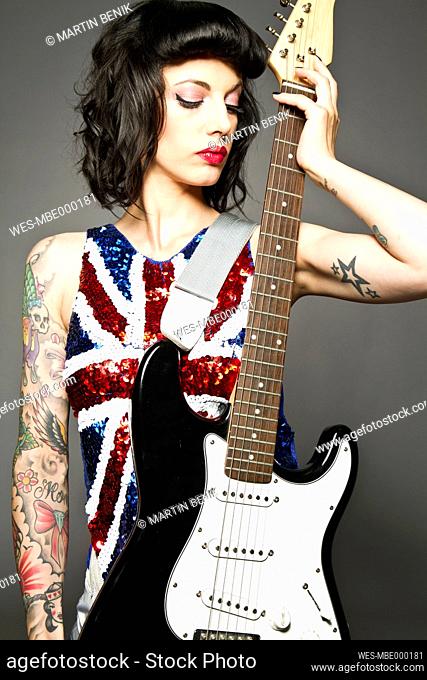 Young woman with guitar and tattoo on her hand against grey background