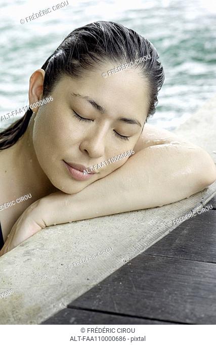 Woman at side of swimming pool resting head on arms