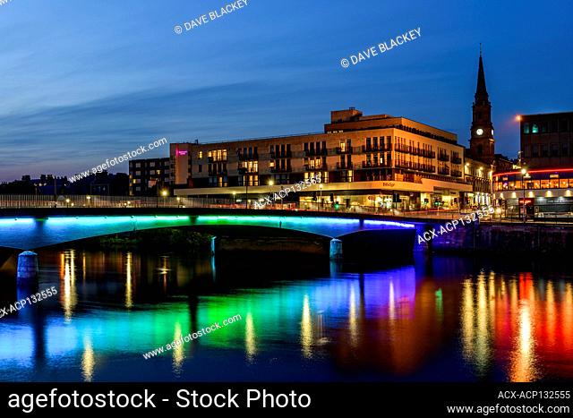 Lights under the Ness Bridge reflect in the River Ness in Inverness, Scotland. The Tollbooth Steeple is in the background