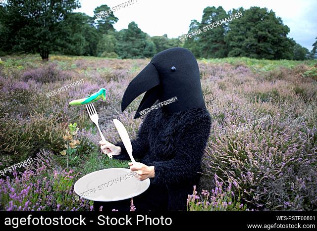 Woman in crow costume eating grasshopper in meadow
