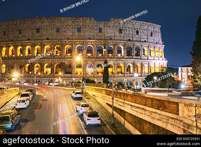 Rome, Italy. Colosseum Also Known As Flavian Amphitheatre In Evening Or Night Time. Night Traffic Light Trails Near Famous World Landmark
