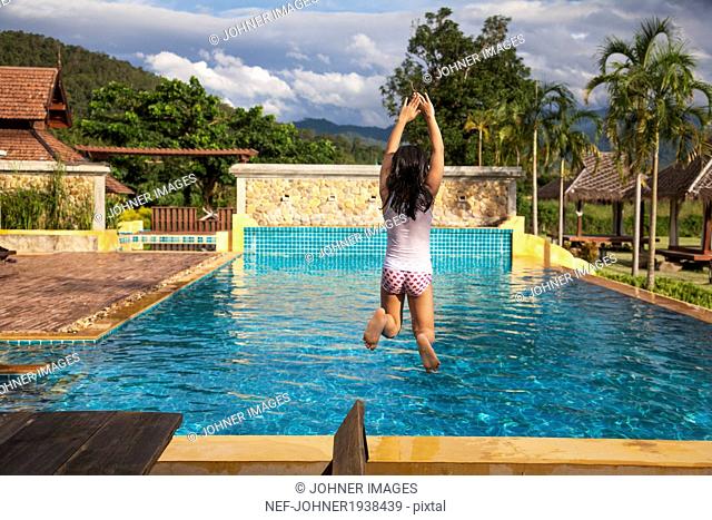 Girl jumping into swimming pool, Thailand